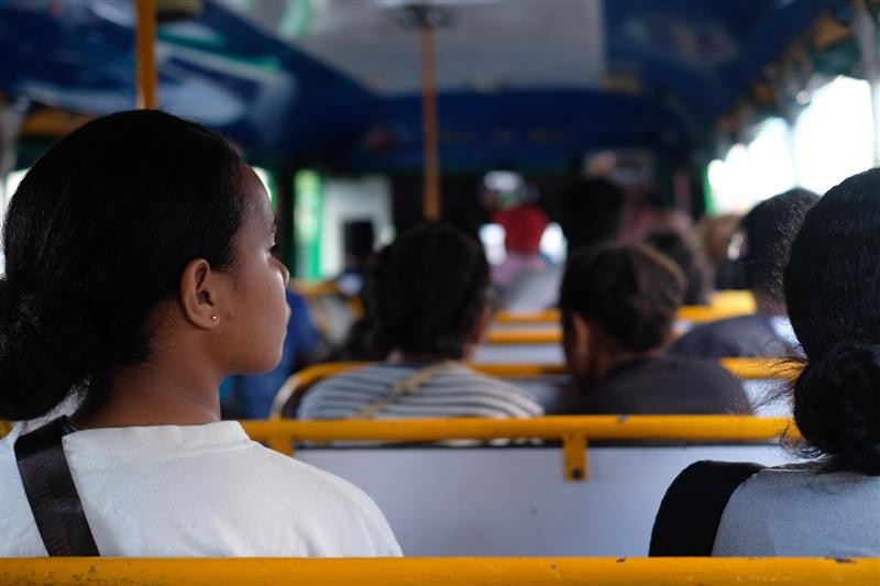 Back shot of young girl on the bus, other passengers in front of her.