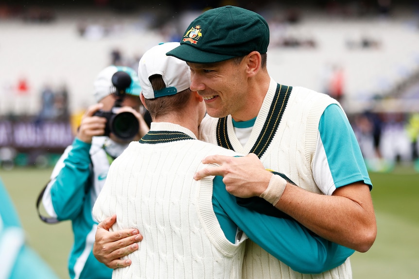 Scott Boland smiles and hugs a teammate wearing a baggy green cap