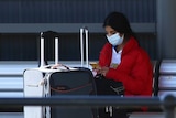 A woman wearing a surgical mask waits for a taxi at Perth Airport.
