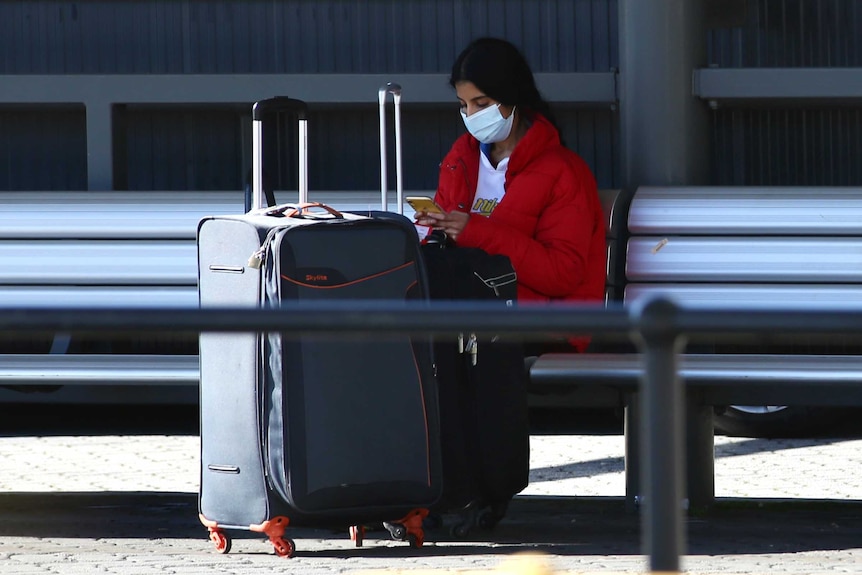 A woman wearing a surgical mask is waiting for a taxi at Perth Airport.