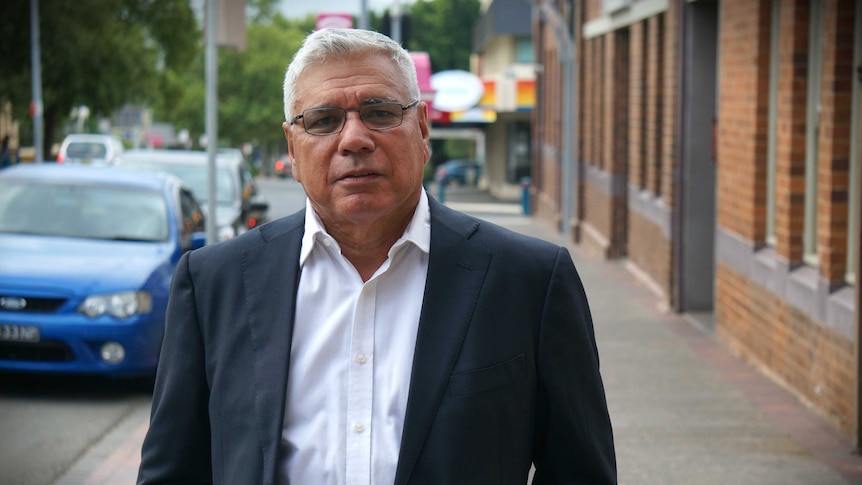 A middle-aged man in a suit jacket stands in a high street