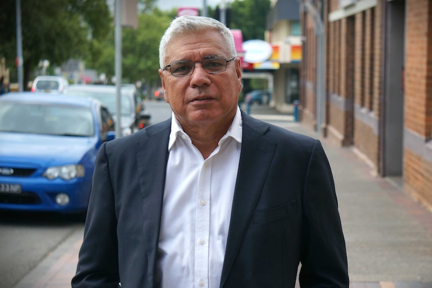 A middle-aged man in a suit jacket stands in a high street