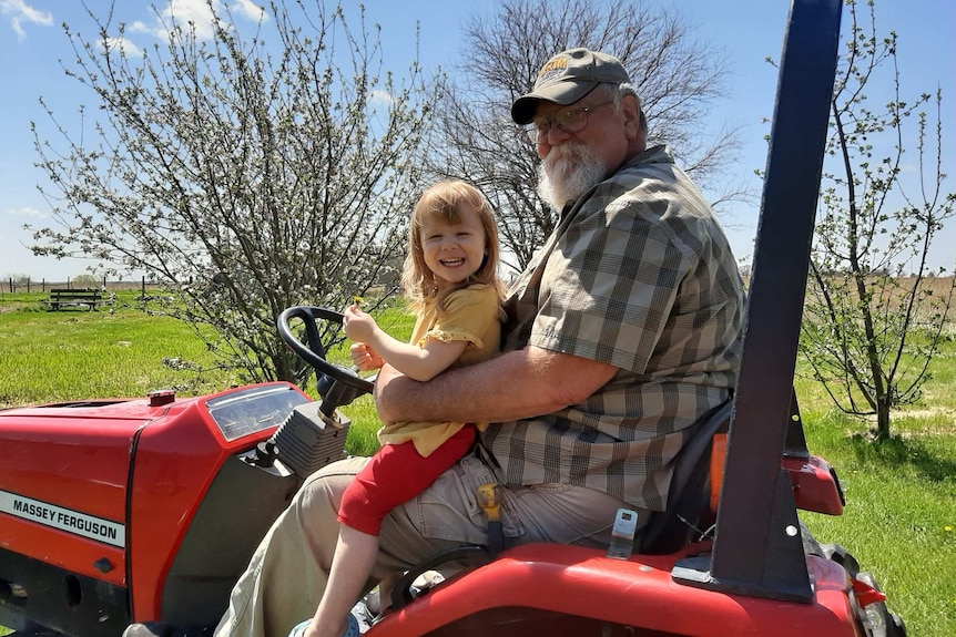 A man sits on a tractor with a smiling toddler in his lap