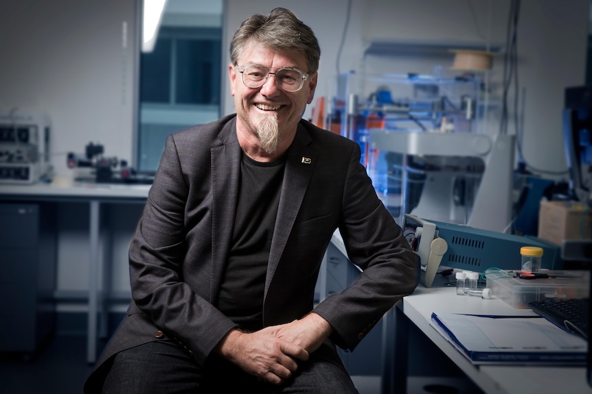 Gordon Wallace sits at a laboratory bench, smiling.