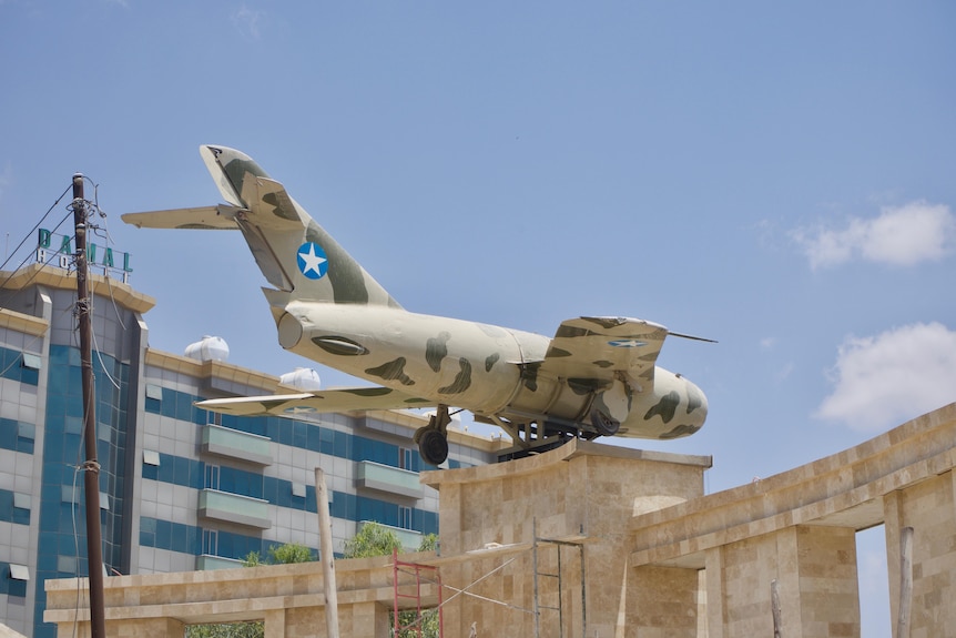 blue sky with a khaki and cream aeroplane displayed on a metal pole.