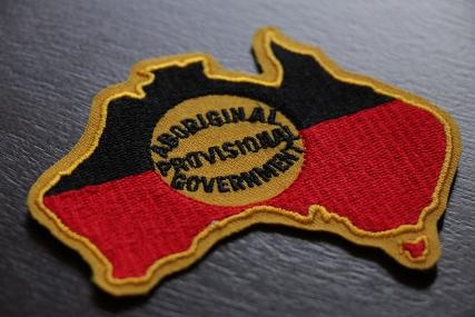 A red, black and yellow Aboriginal flag in the shape of Australia with Aboriginal Provisional Government written in the centre.