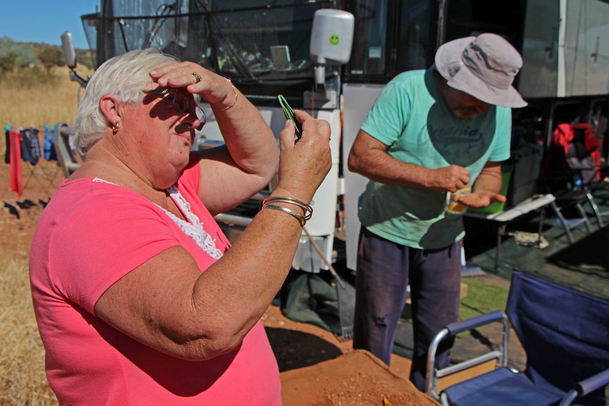 A woman and man use tweezers to inspect rocks for gemstones.