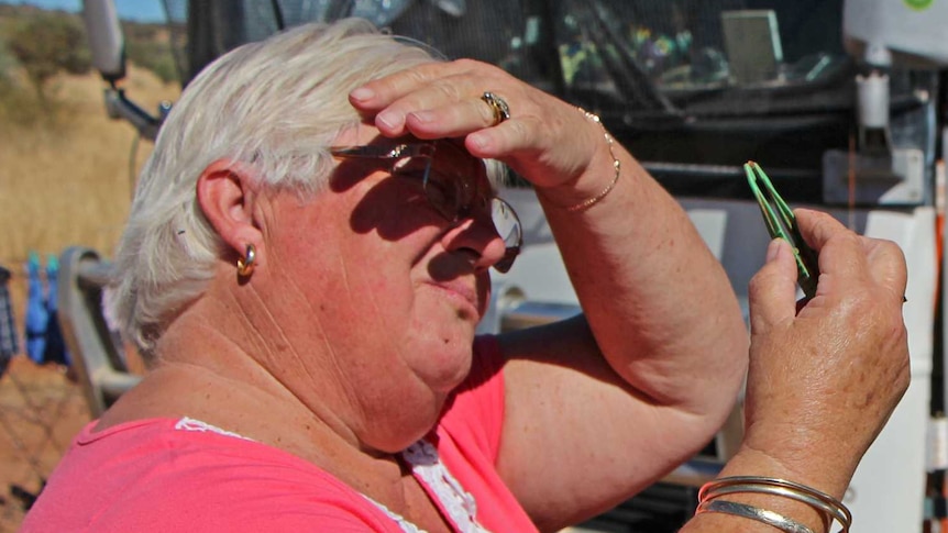 A woman and man use tweezers to inspect rocks for gemstones.