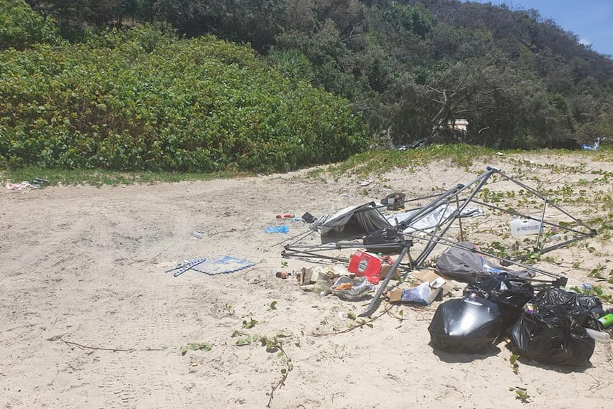 Landscape shot of Teewah Beach showing broken camping tent, empty beer packets and rubbish bags.