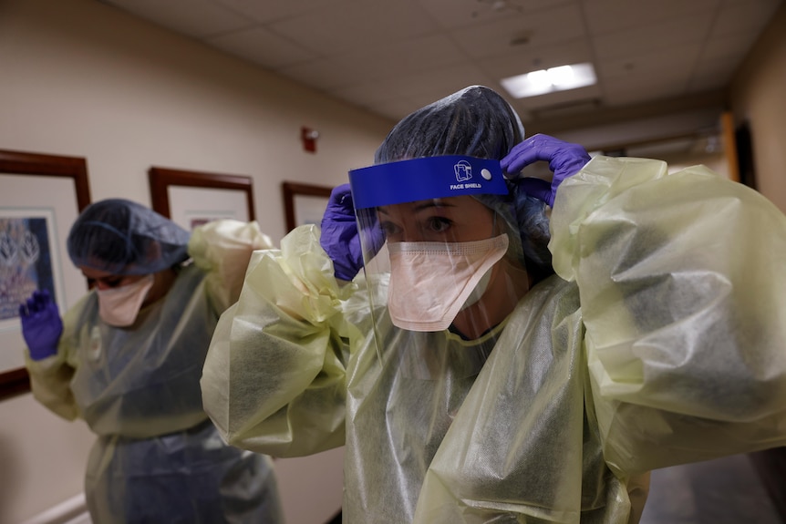 Nurses in gowns, caps gloves, putting on their face shields as they walk down the corridor