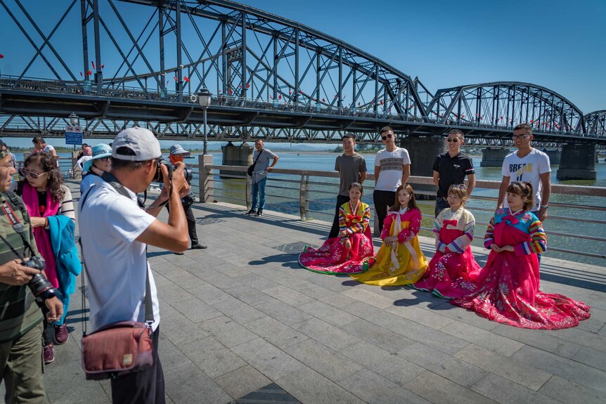 Four Chinese tourists pose with four North Korean waitresses as another man takes their photo.
