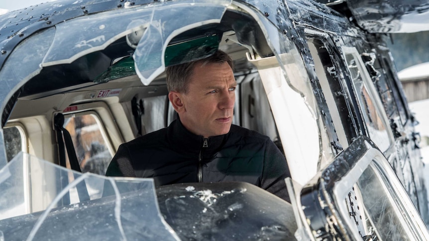 Daniel Craig, as James Bond, peers out a shattered helicopter window with a worried look on his face