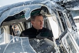Daniel Craig, as James Bond, peers out a shattered helicopter window with a worried look on his face