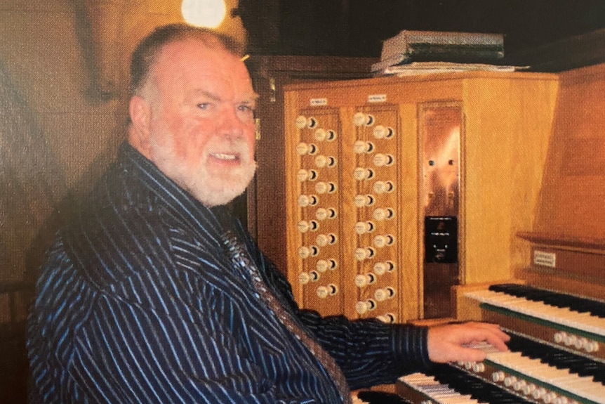 An older man sitting at the keyboards of a large pipe organ.