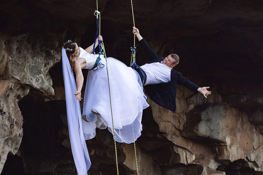 A couple abseiling in their wedding clothes.