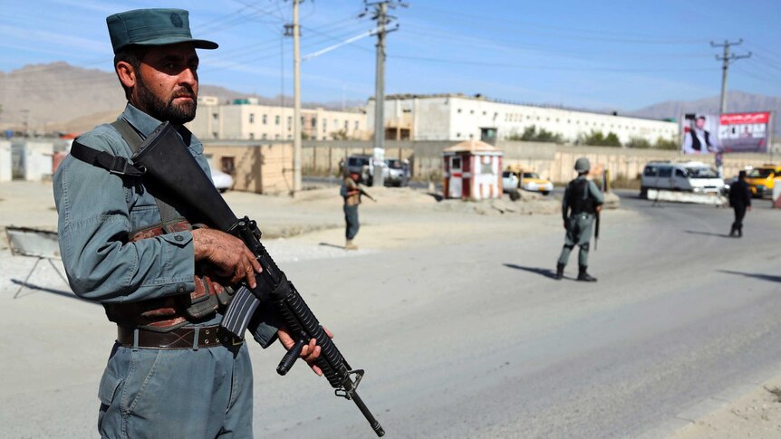 A man in police uniform stands holding a gun in Afghanistan.