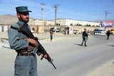 A man in police uniform stands holding a gun in Afghanistan.