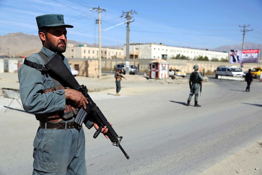 A man in police uniform stands holding a gun in Afghanistan.