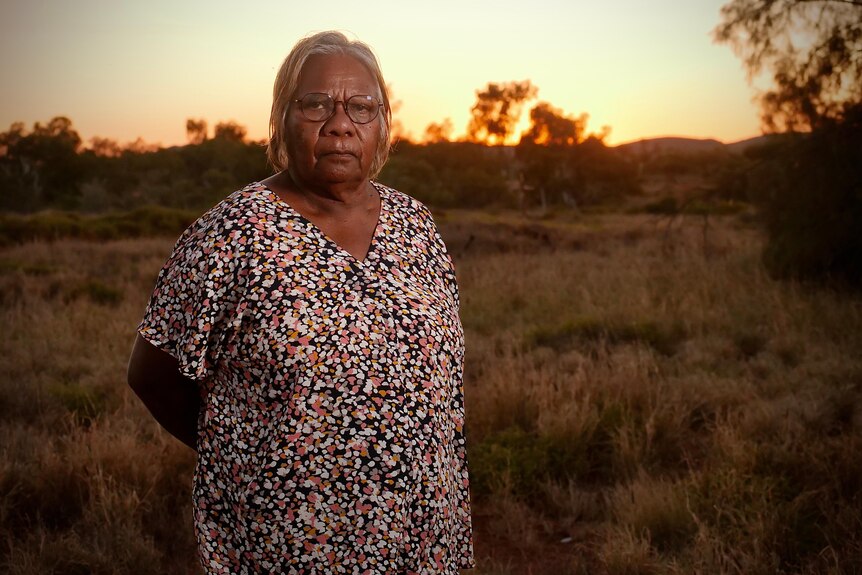 Older Aboriginal women, wearing reading glasses and a floral shirt standing in the bush at sunset