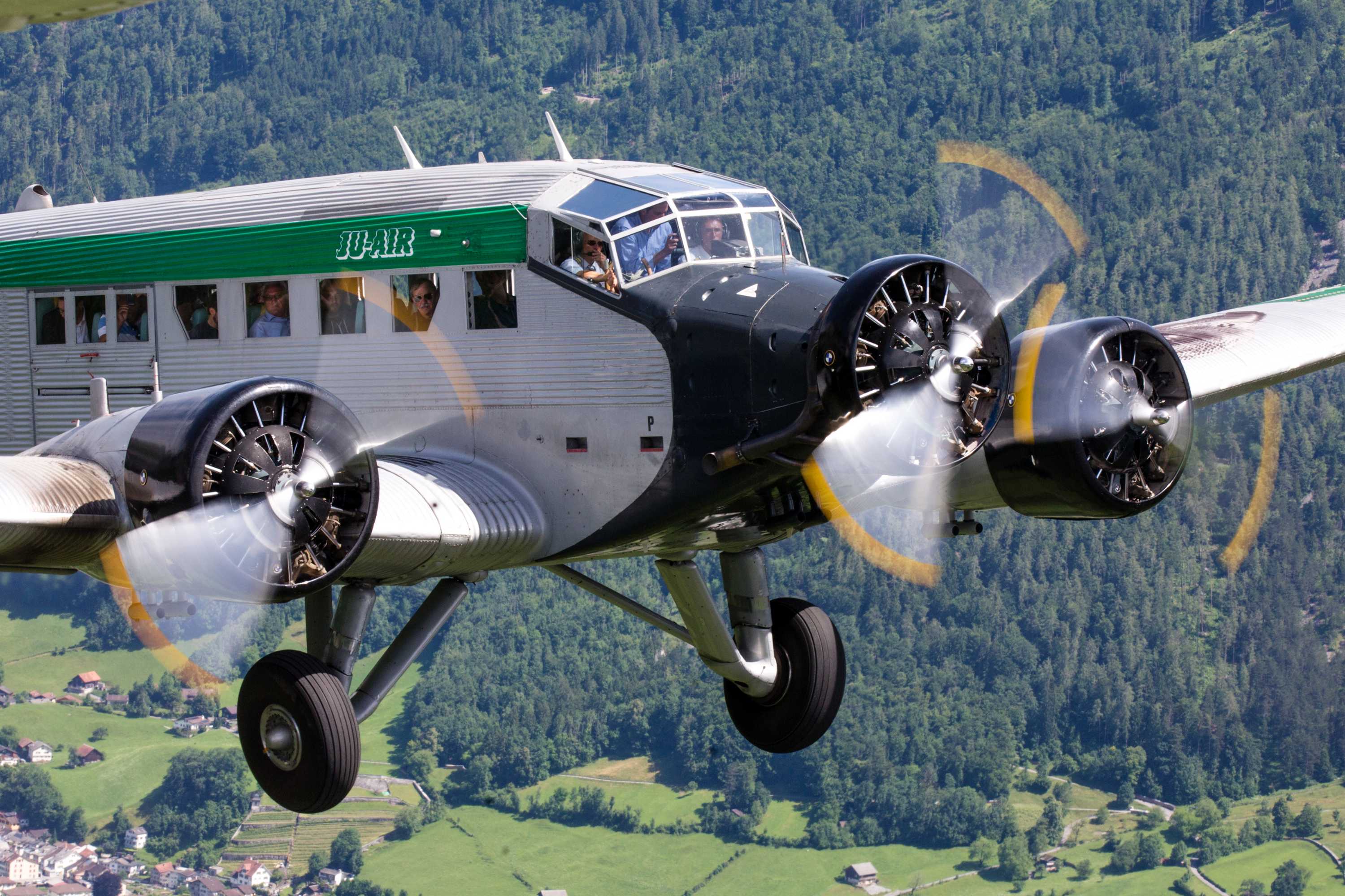 Passengers looking out of the JU-52 aircraft as it flies in the sky.
