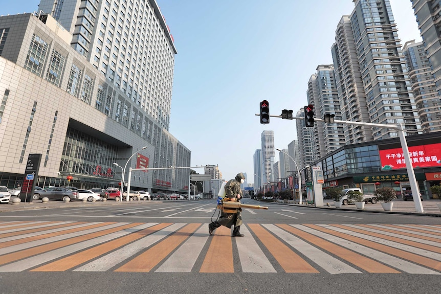 On a clear day, you look up at silver skyscrapers as a person covered head-to-toe carries a long metal disinfectant machine.