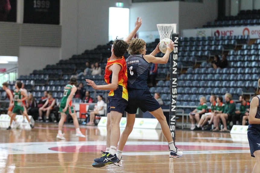 Zac in blue uniform and centre bib landing with ball next to boy in red and yellow uniform with his arm up 