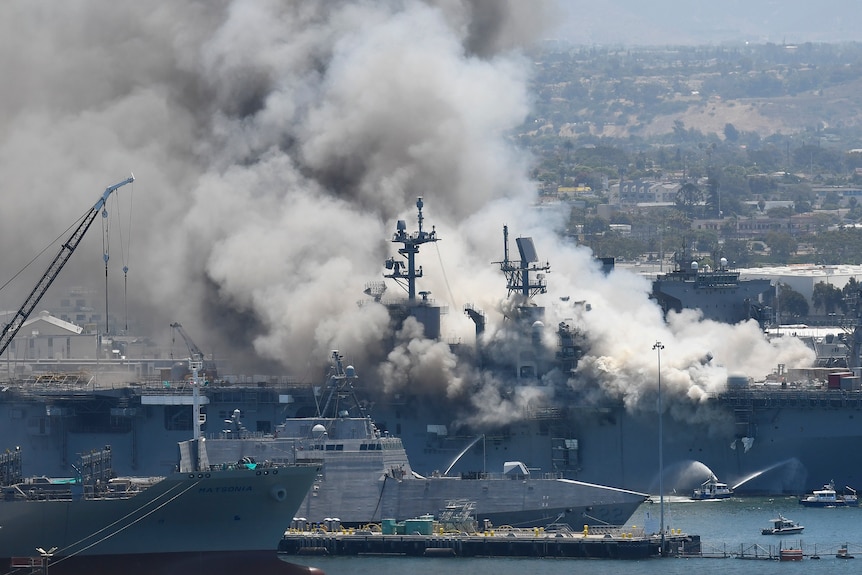 Smoke plumes from a large naval ship in a shipyard.