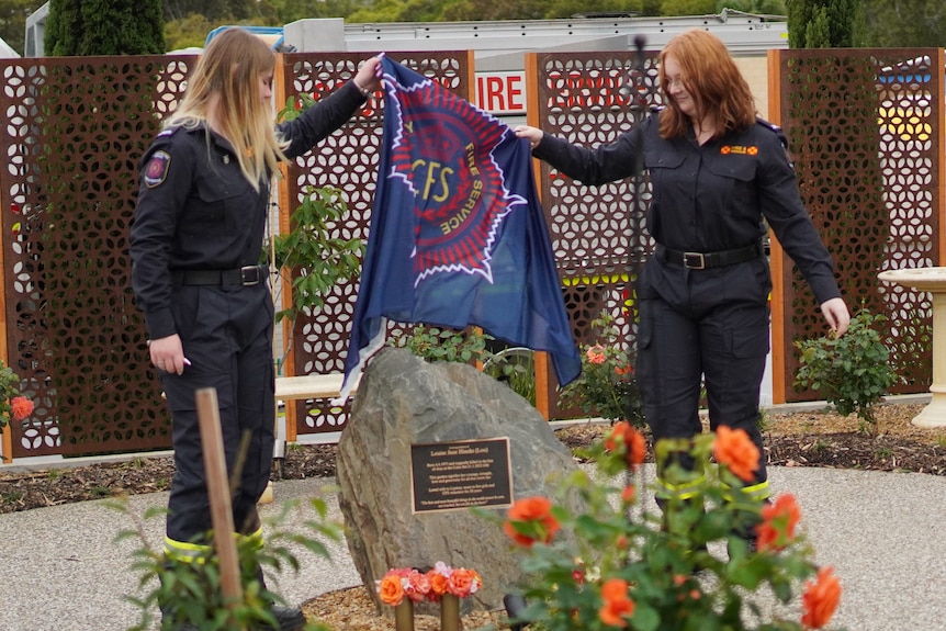 Two young women lift a CFS flag from a memorial stone
