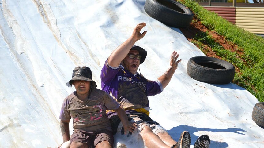 A man and a boy slide down a soapy slide.