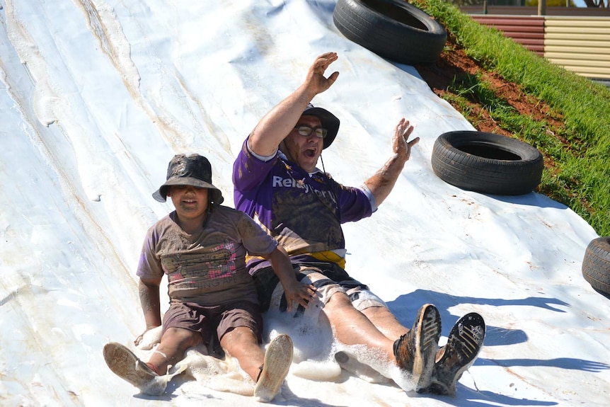 A man and a boy slide down a soapy slide.