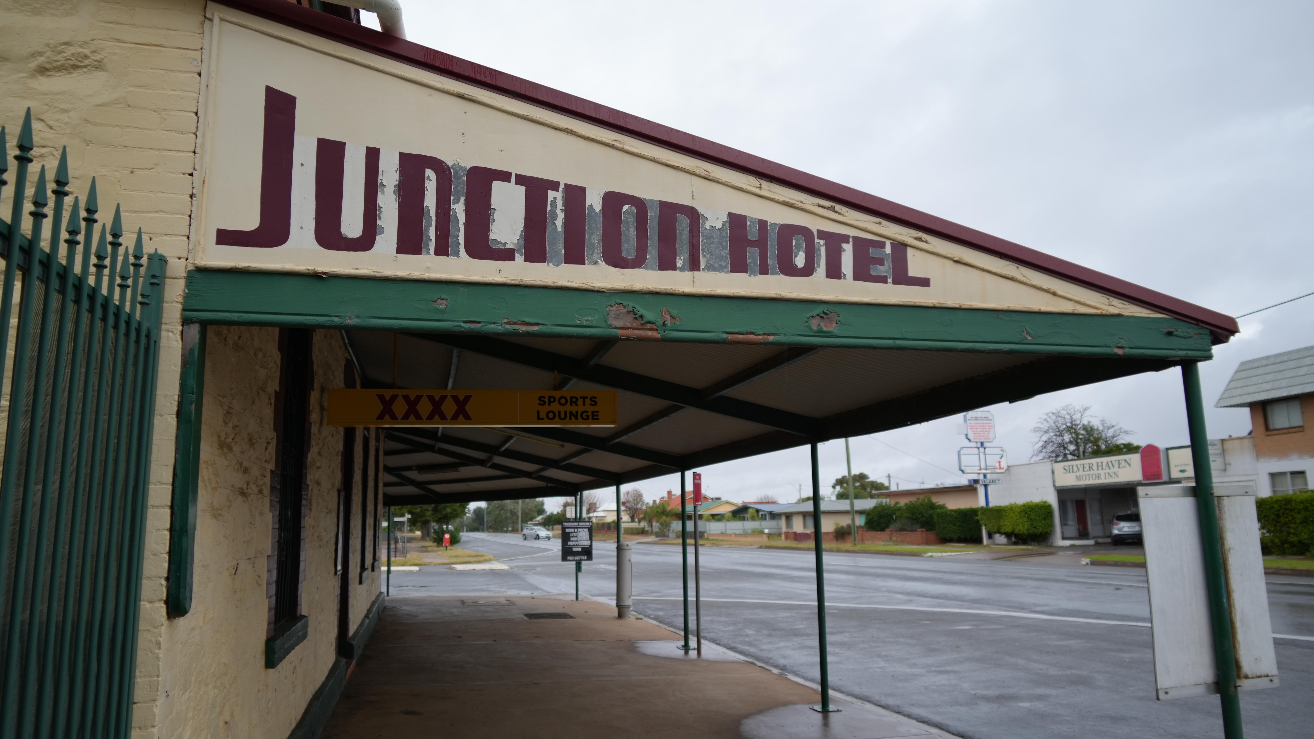 A cream coloured building with an awning stretching out over a sidewalk which reads Junction Hotel