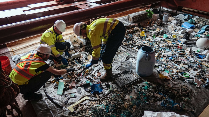 Crew members sift through plastic laid out on a canvas collected by a floating ocean boom