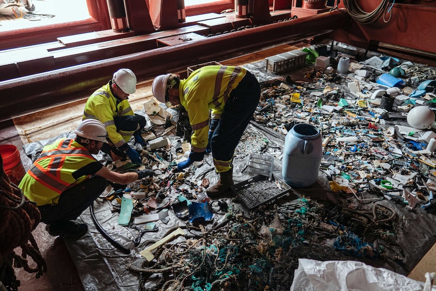 Crew members sift through plastic laid out on a canvas collected by a floating ocean boom
