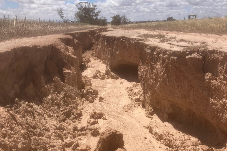 A dirt road with a large gully running through the centre of it after being damaged by water