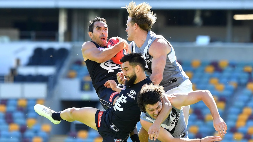 An AFL player grimaces as he takes a pack mark with other players colliding in mid-air.