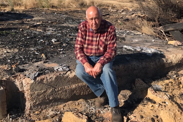 A farmer sitting on an ashen  pile of rubble