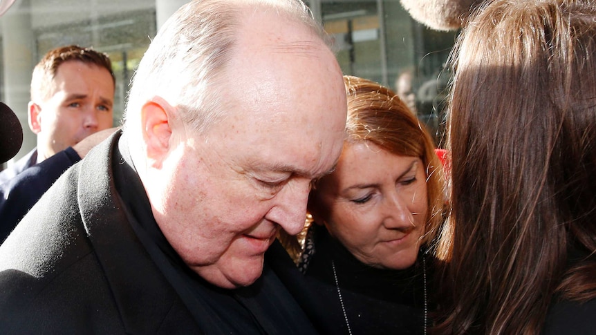 Archbishop Philip Wilson bows his head as he walks through a media scrum outside court
