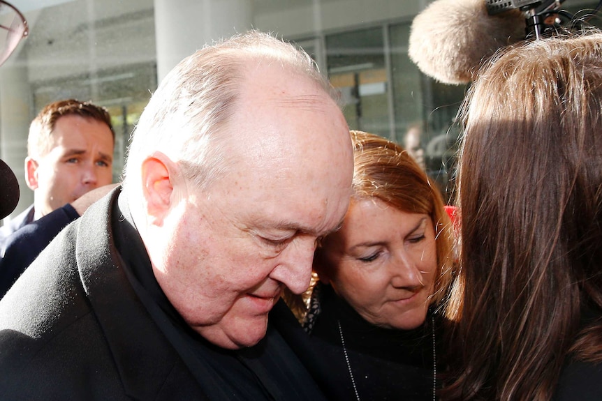 Archbishop Philip Wilson bows his head as he walks through a media scrum outside court