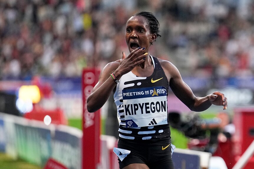 A woman puts her hand to her mouth in shock as she crosses a finish line.