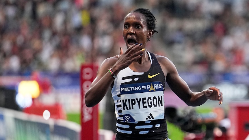 A woman puts her hand to her mouth in shock as she crosses a finish line.