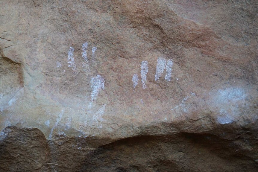 White chalk prints from climbers on a rock wall near some rock art