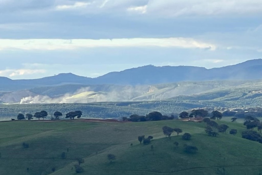 Plumes of dust rising off the site of a mine with hills in the foreground and background 