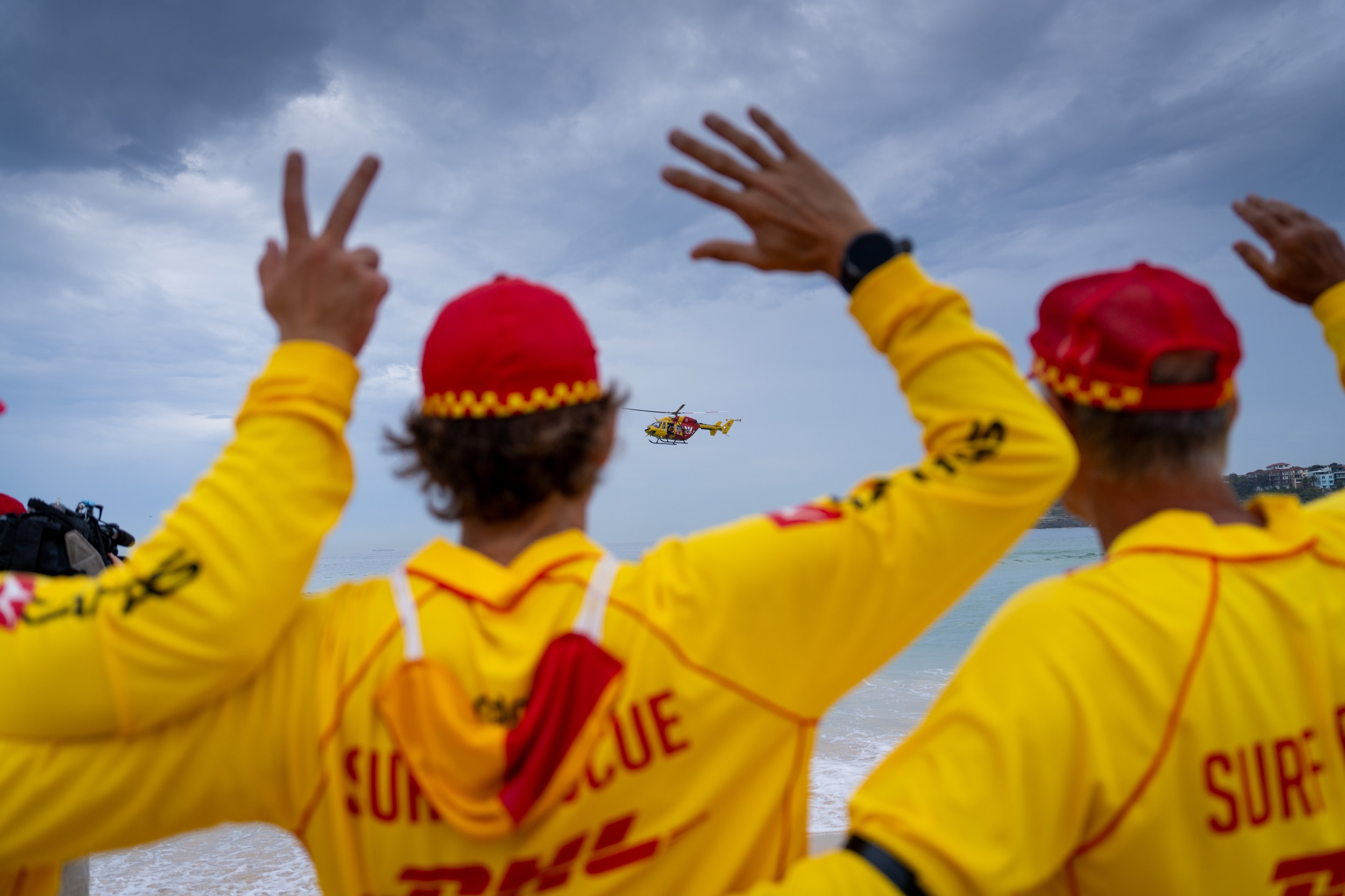 Salva-vidas do surf cumprimentam um helicóptero Westpac sobrevoando o mar