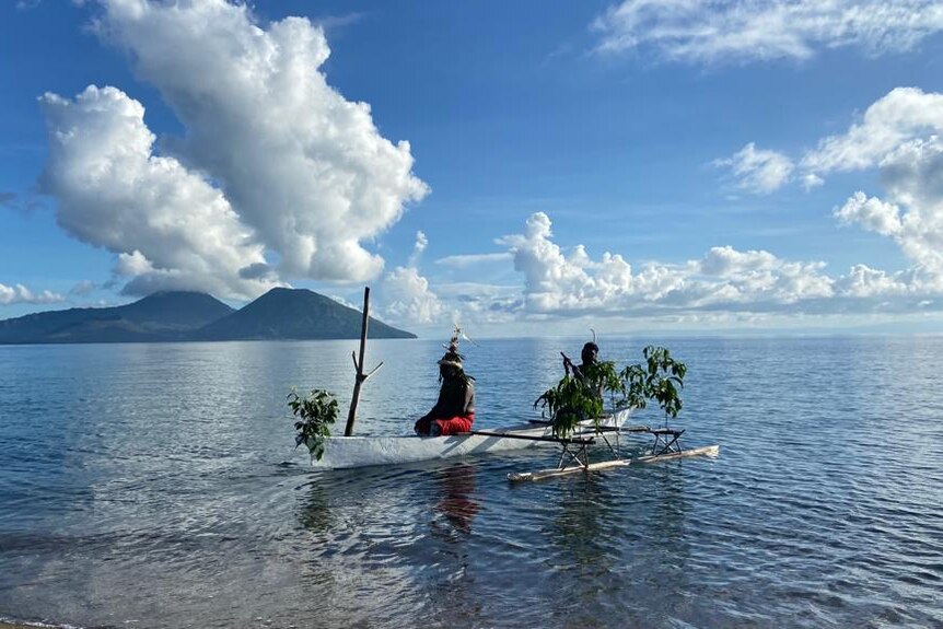 Two men in a traditional pacific island canoe arriving to shore with volcano in the distant background.