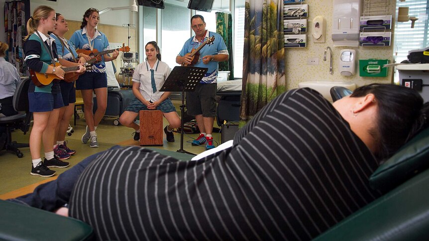 A patient lays down on a recliner while the Ukulele Angels perform in the oncology ward of Cairns Hospital.