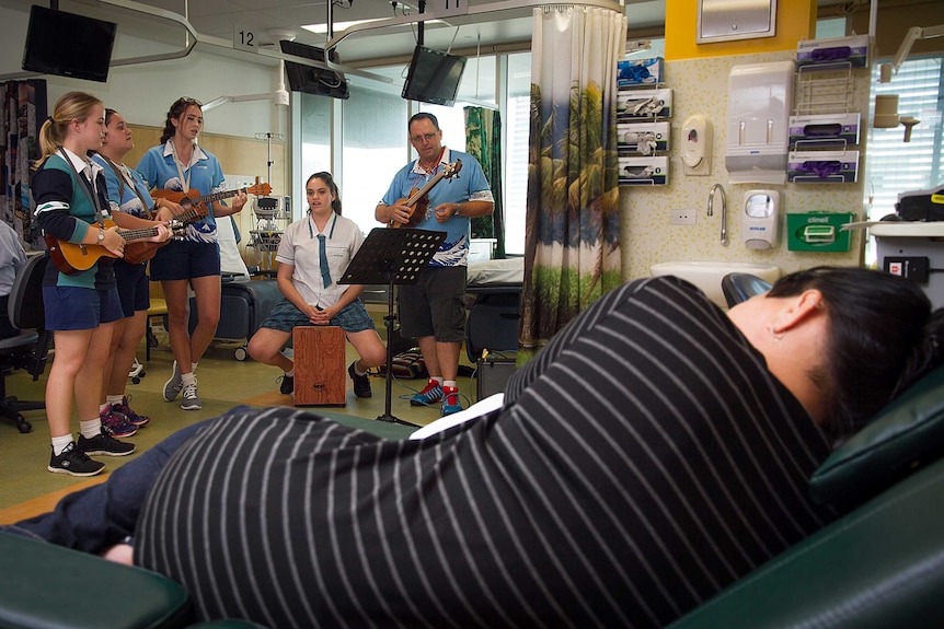 A patient lays down on a recliner while the Ukulele Angels perform in the oncology ward of Cairns Hospital.