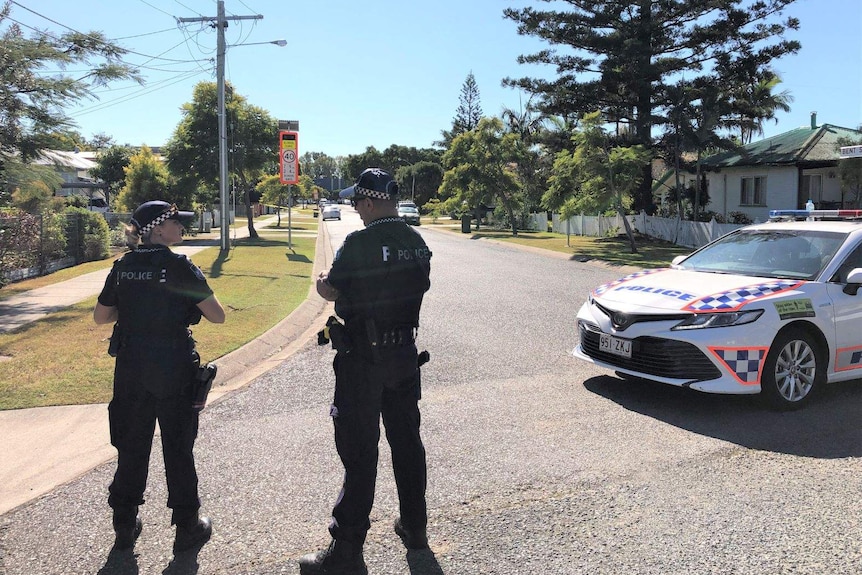 Two police stand near a police car on a suburban street