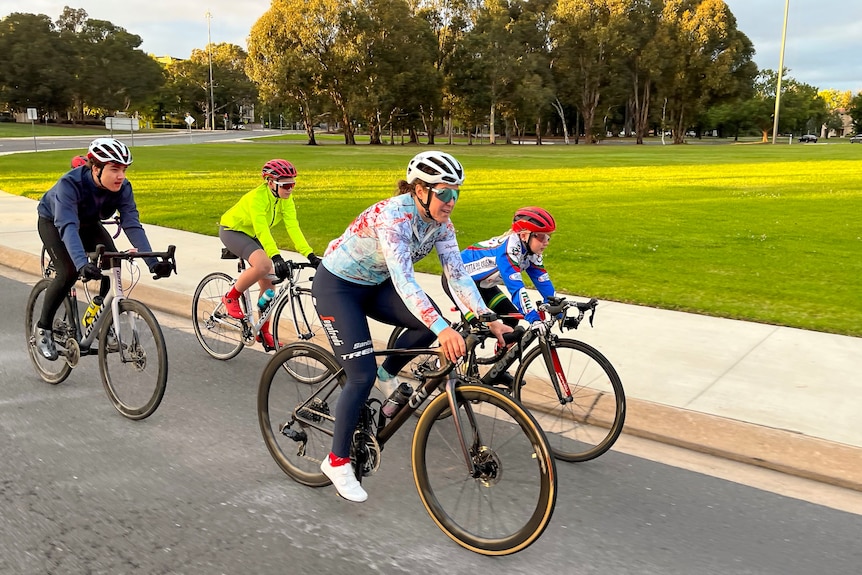 Woman cycling with a group of children on the road. 