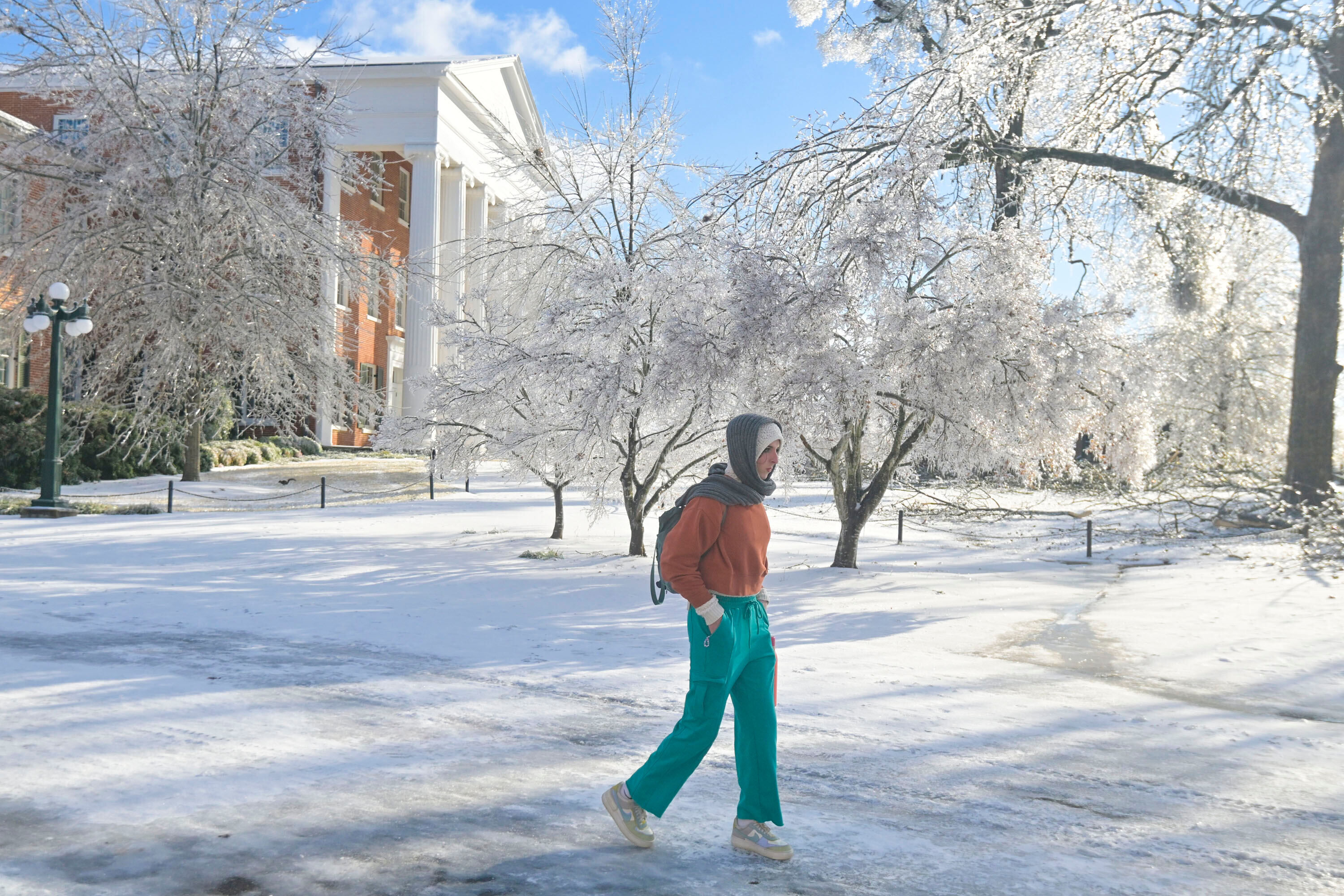Una mujer camina por una calle helada frente a un campus universitario y árboles cubiertos de nieve.