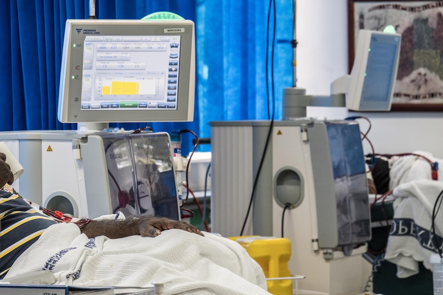 An Indigenous man in a hospital bed linked to a dialysis chair.